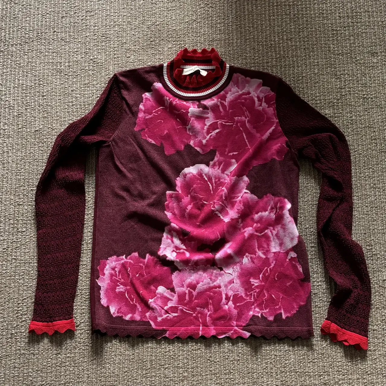 Sweater de cuello alto con estampado floral en tonos rosa y mangas largas. Detalles en rojo en el cuello, puños y borde inferior. Ideal para un look casual y con estilo.