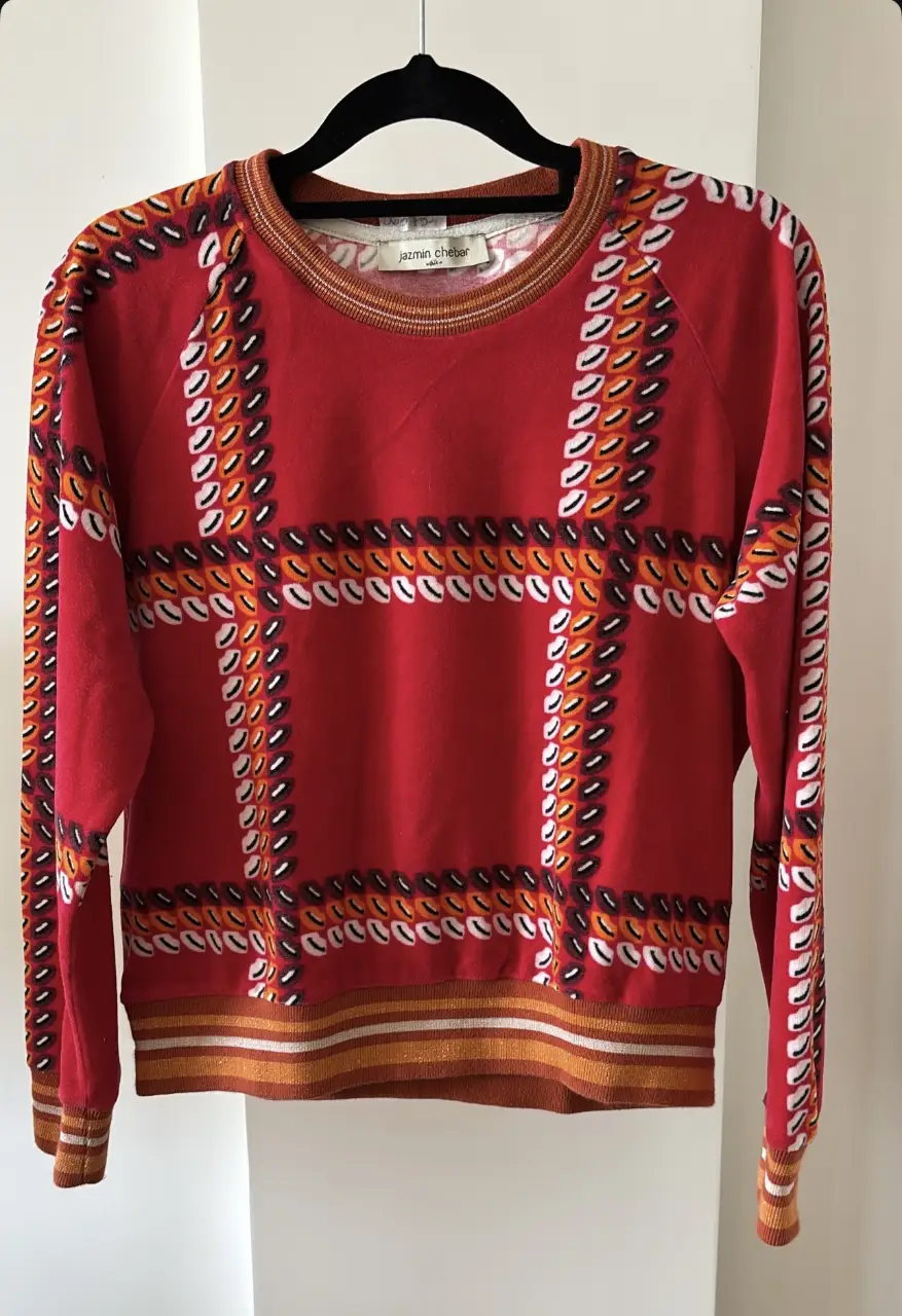 Buzo de cuello redondo Jazmin Chebar, rojo con diseño geométrico en blanco, naranja y negro. Detalles en el cuello y puños.