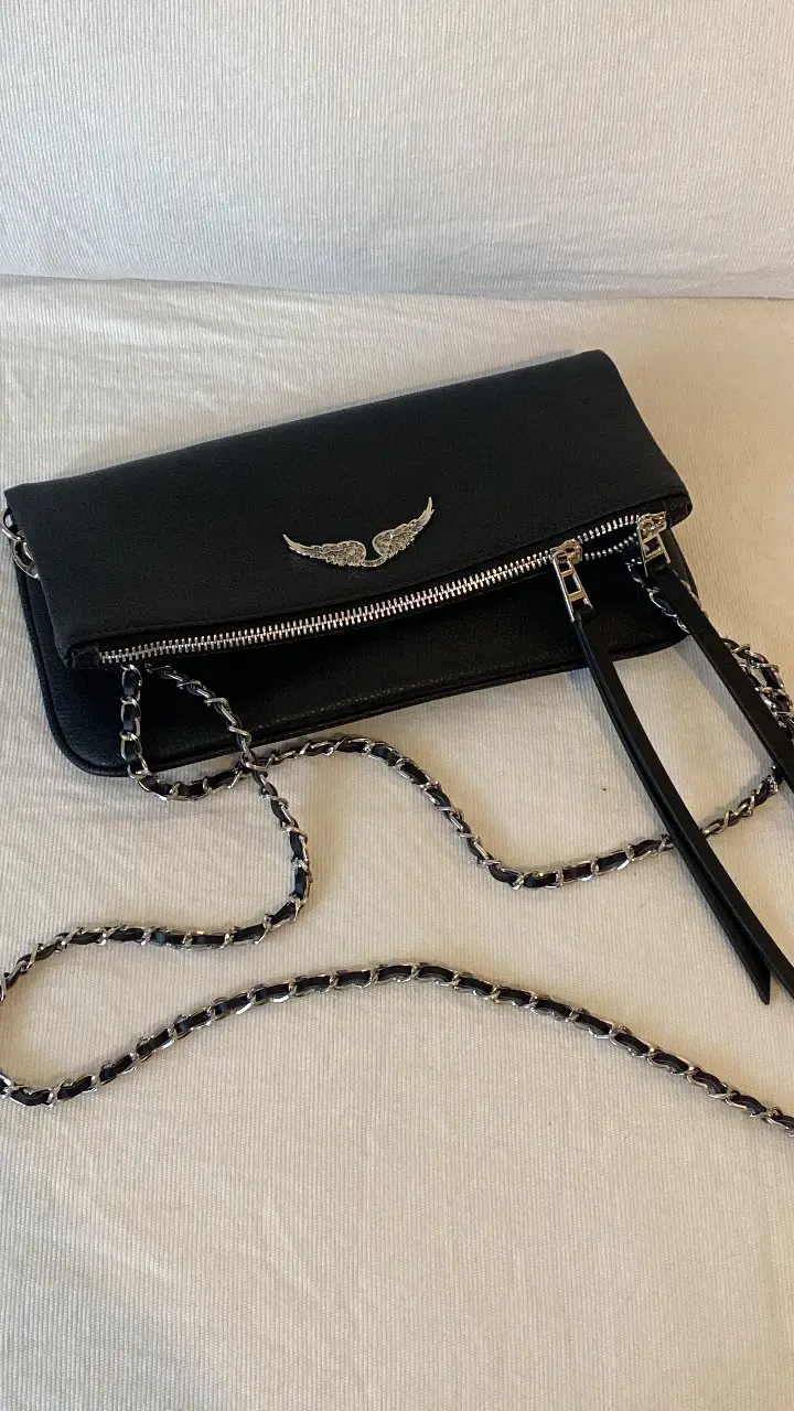 Cartera bandolera negra con cadena plateada y detalle de alas plateadas. Ideal para salidas y eventos. Con bolsa guarda polvo 