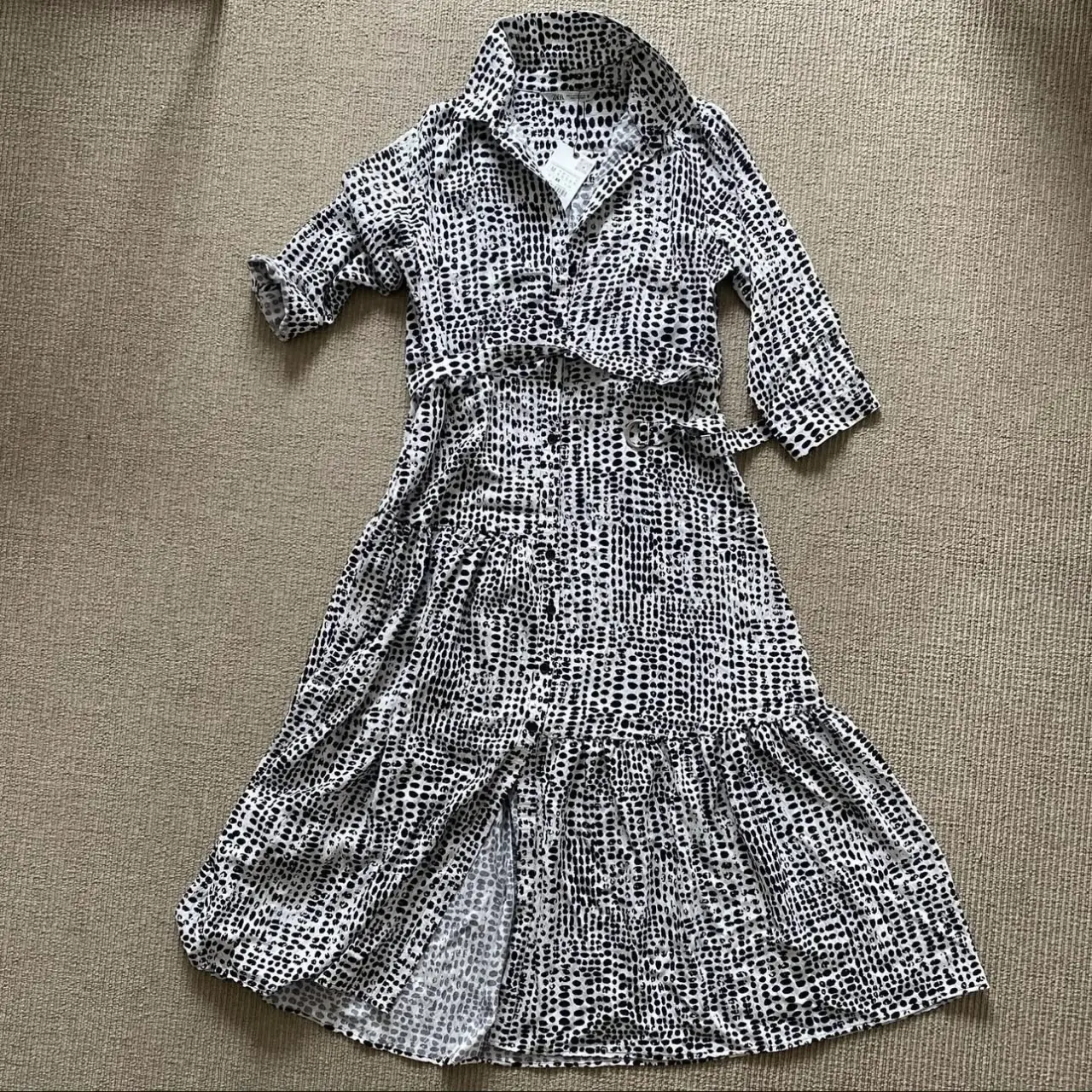 Vestido midi con estampado de lunares en blanco y negro. Diseño camisero con cuello, botones delanteros y cinturón para ajustar la cintura. Mangas 3/4 y falda con volados.