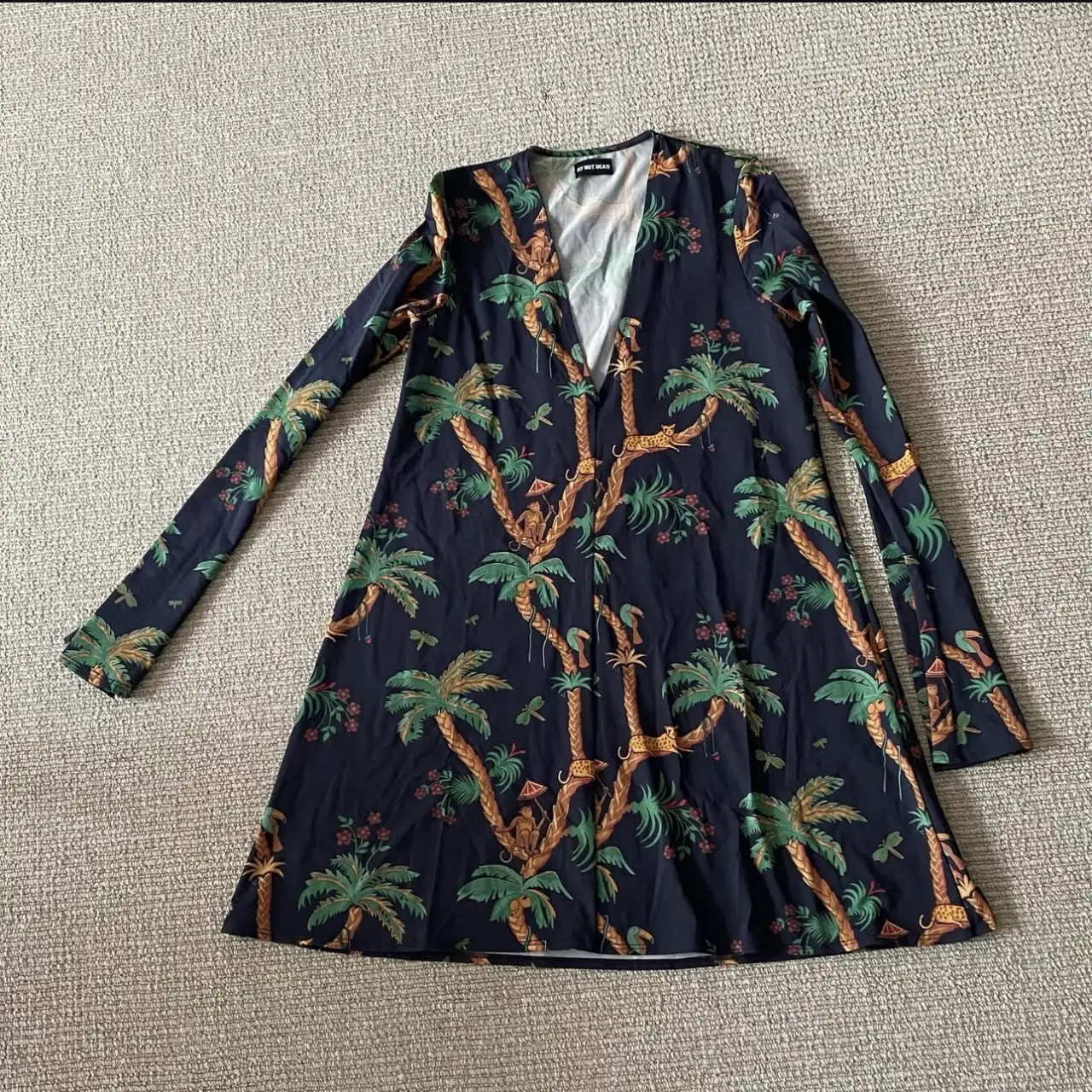 Vestido mini con estampado de palmeras y animales en tonos verdes y marrones sobre fondo azul oscuro. Cuello en V y mangas largas.