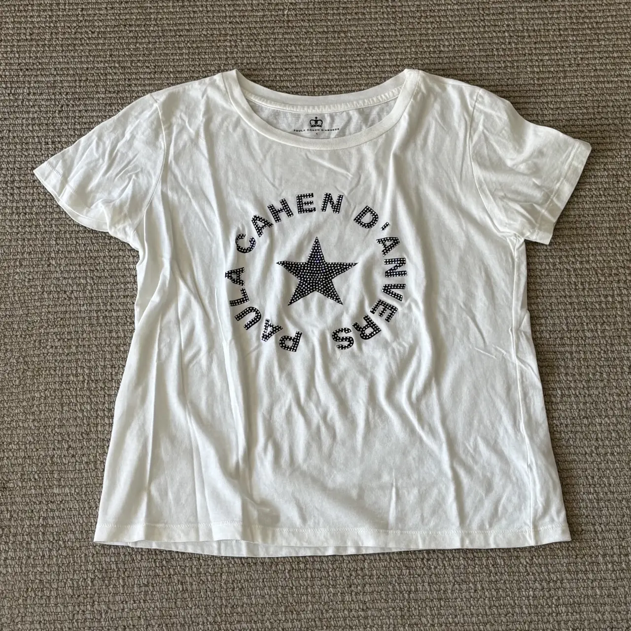 Remera blanca de mujer con estampado "CAHEN D'ANVERS" con brillos y estrella en el centro. Cuello redondo y manga corta. Ideal para un look casual y moderno.