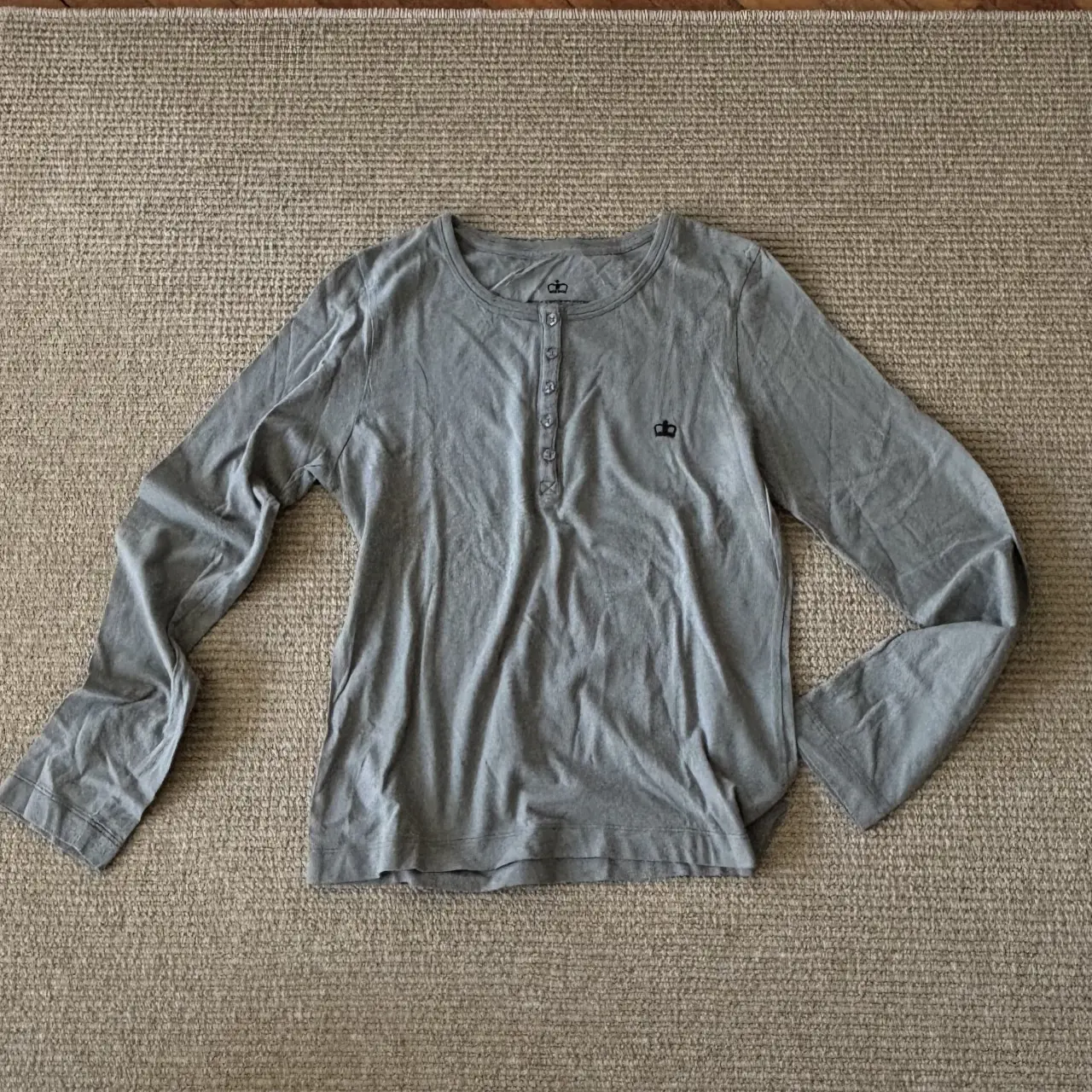 Remera manga larga gris con botones en el cuello y logo de corona bordado. Ideal para un look casual y cómodo.
