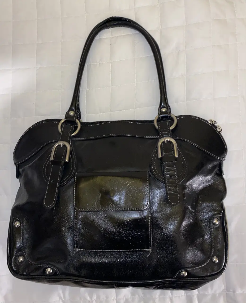 Cartera negra de cuero sintético con manijas y detalles plateados. Posee un bolsillo frontal y un interior espacioso con bolsillos adicionales. Ideal para un look elegante y funcional.