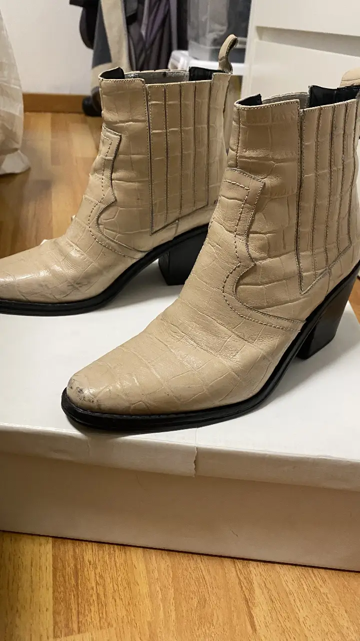 Botas de cuero  color crema. Tienen un tacón negro y un estilo cowboy moderno. Ideales para un look casual y a la moda.