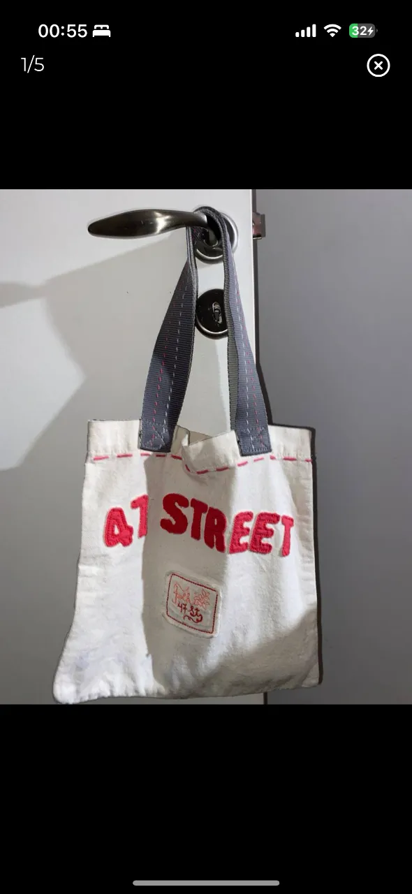 Bolso tote bag de lona blanca con estampado "A1 STREET" en rojo. Tiene manijas grises y detalles de costura en rojo. Ideal para un look casual y urbano.