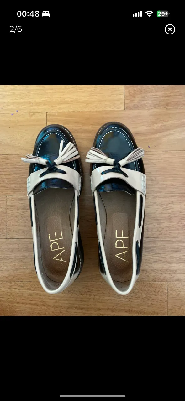 Mocasines de cuero charol negro con detalles en blanco y borlas. Ideales para un look preppy y elegante.