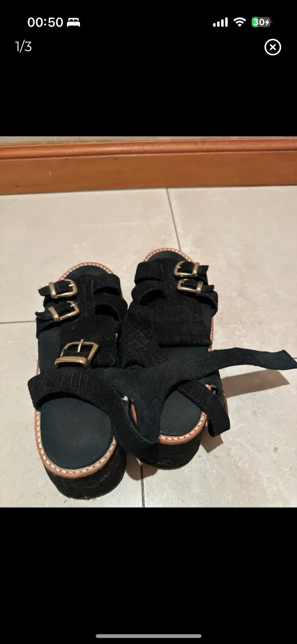 Sandalias negras con plataforma y hebillas doradas, ideales para un look moderno y cómodo. Perfectas para combinar con diferentes outfits.