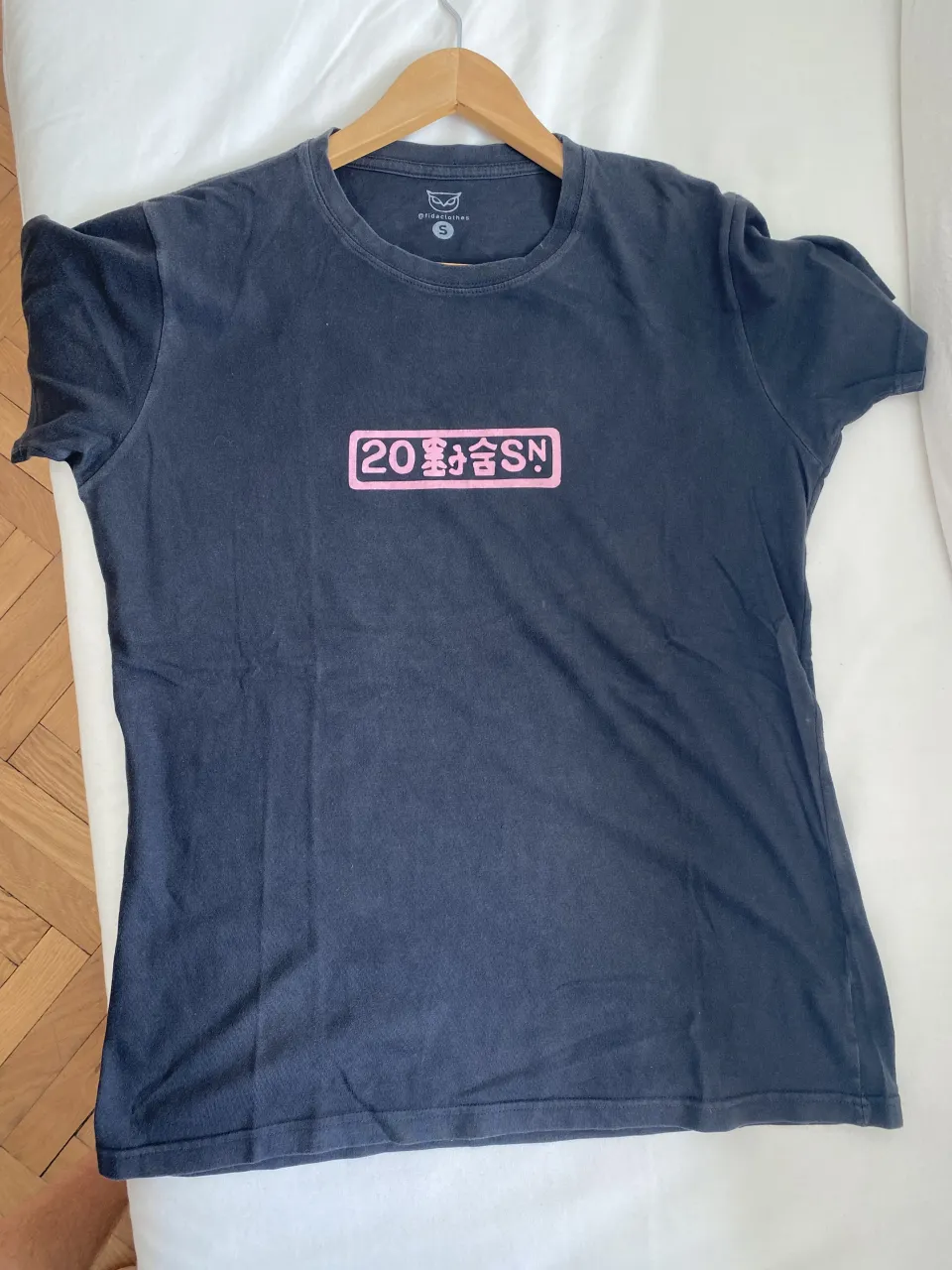 Remera negra con estampa frontal y trasera en color rosa. La estampa frontal tiene un recuadro con texto y un logo. La estampa trasera tiene un diseño inspirado en arte japonés con una montaña, un ciervo y un sol naciente.