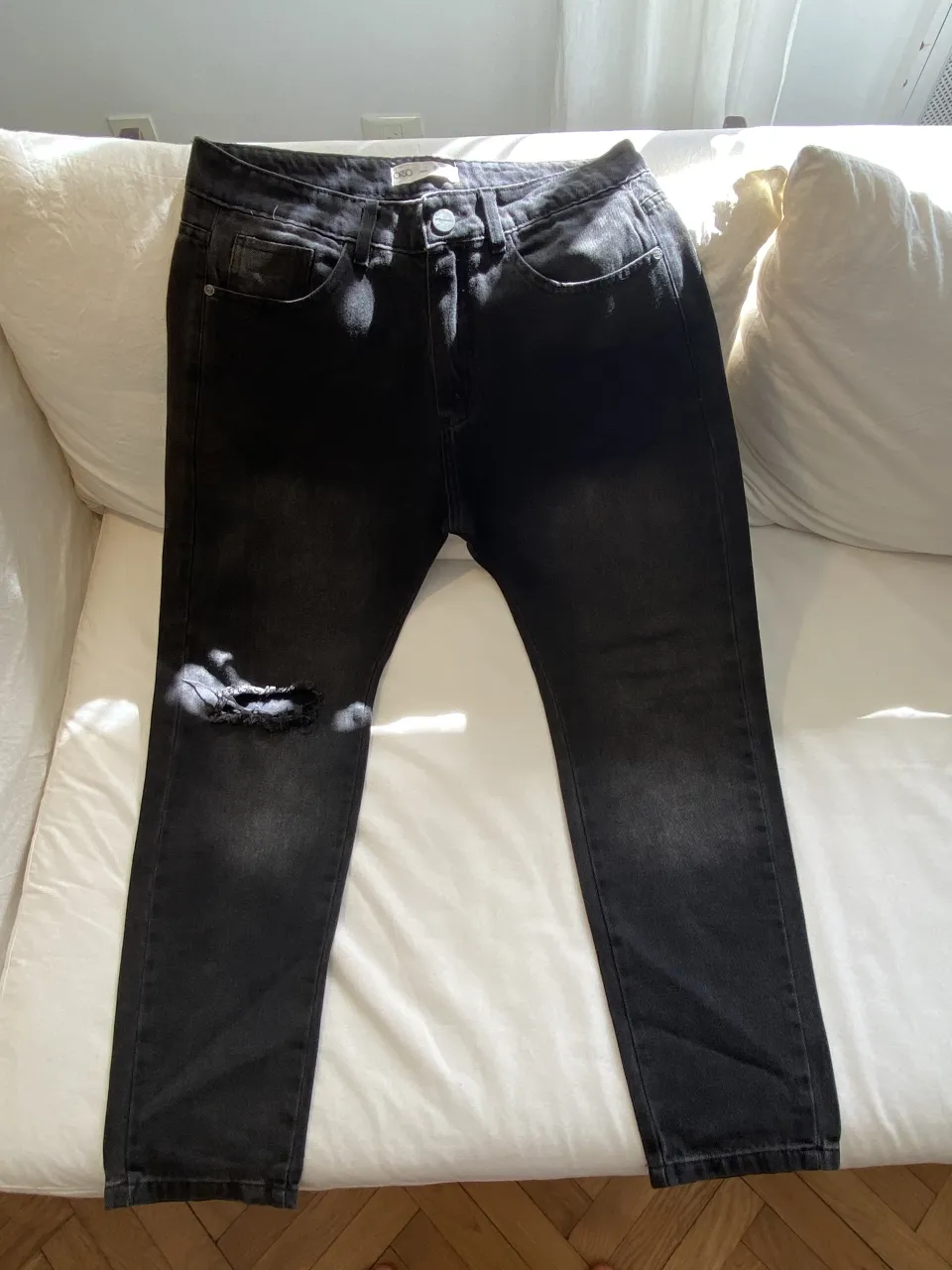 Jean negro con rotura en la rodilla izquierda. Cierre de botón y bolsillos delanteros y traseros.