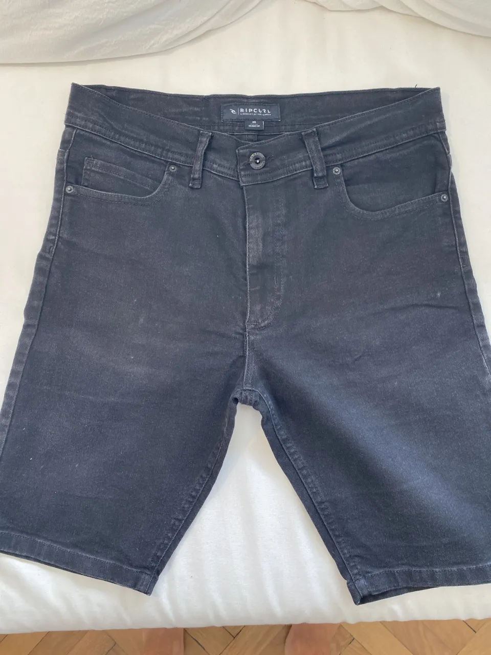 Shorts de jean negros, tiro medio, con cinco bolsillos. Cierre con botón y abrojo.