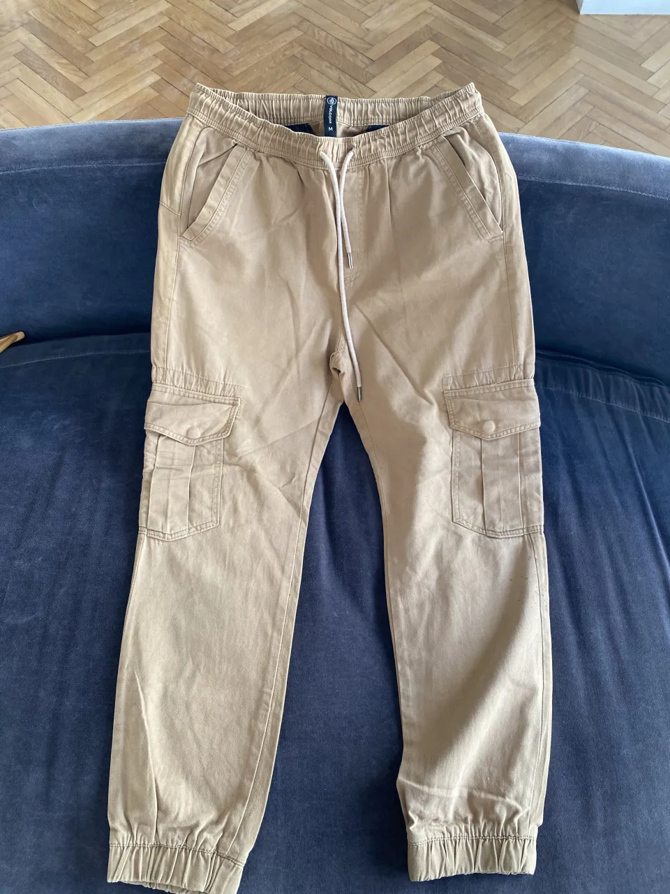 Pantalón cargo de color beige con cordón blanco en la cintura y bolsillos laterales.