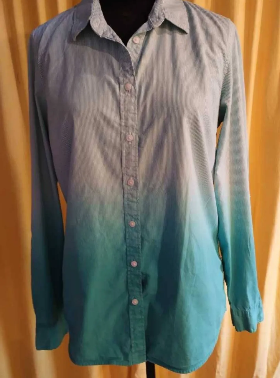 Camisa de manga larga con un degradado de color celeste a verde. Tiene botones al frente y un pequeño logo de la marca en la manga. Ideal para un look casual y fresco.