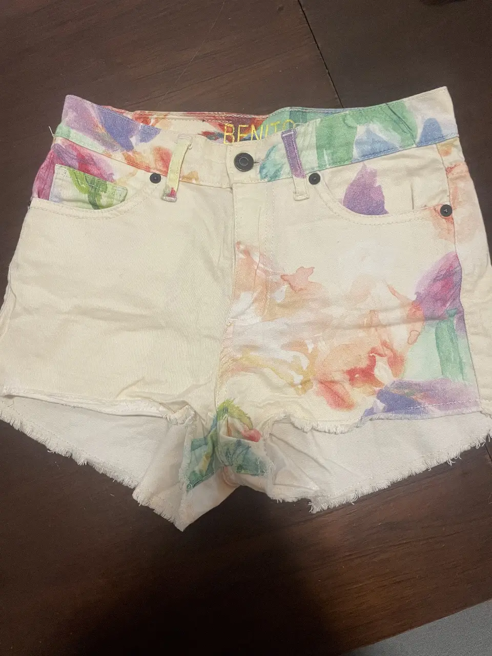 Short de jean de mujer con estampado de colores en tonos pastel. Tiro medio, con detalles de flecos en el borde inferior. Ideal para un look casual y fresco.