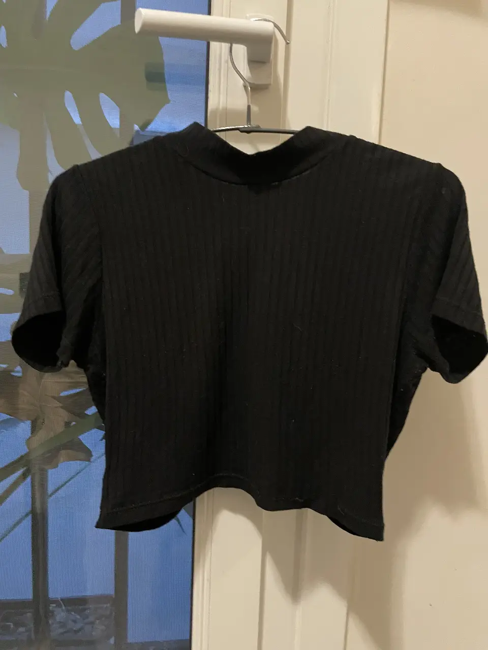 Top negro de cuello alto y manga corta, ideal para un look moderno y versátil. Confeccionado en tejido de punto acanalado. Posee la espalda abierta con tiras para hacer un nudo.
