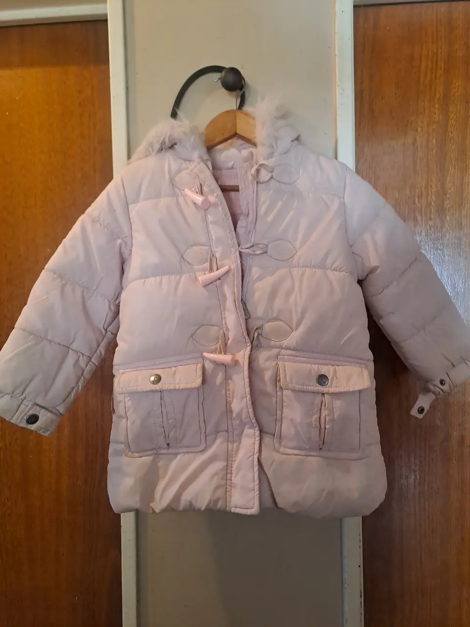Campera de pluma para niña, color rosa claro, con capucha y detalles de botones de madera. Ideal para el invierno.