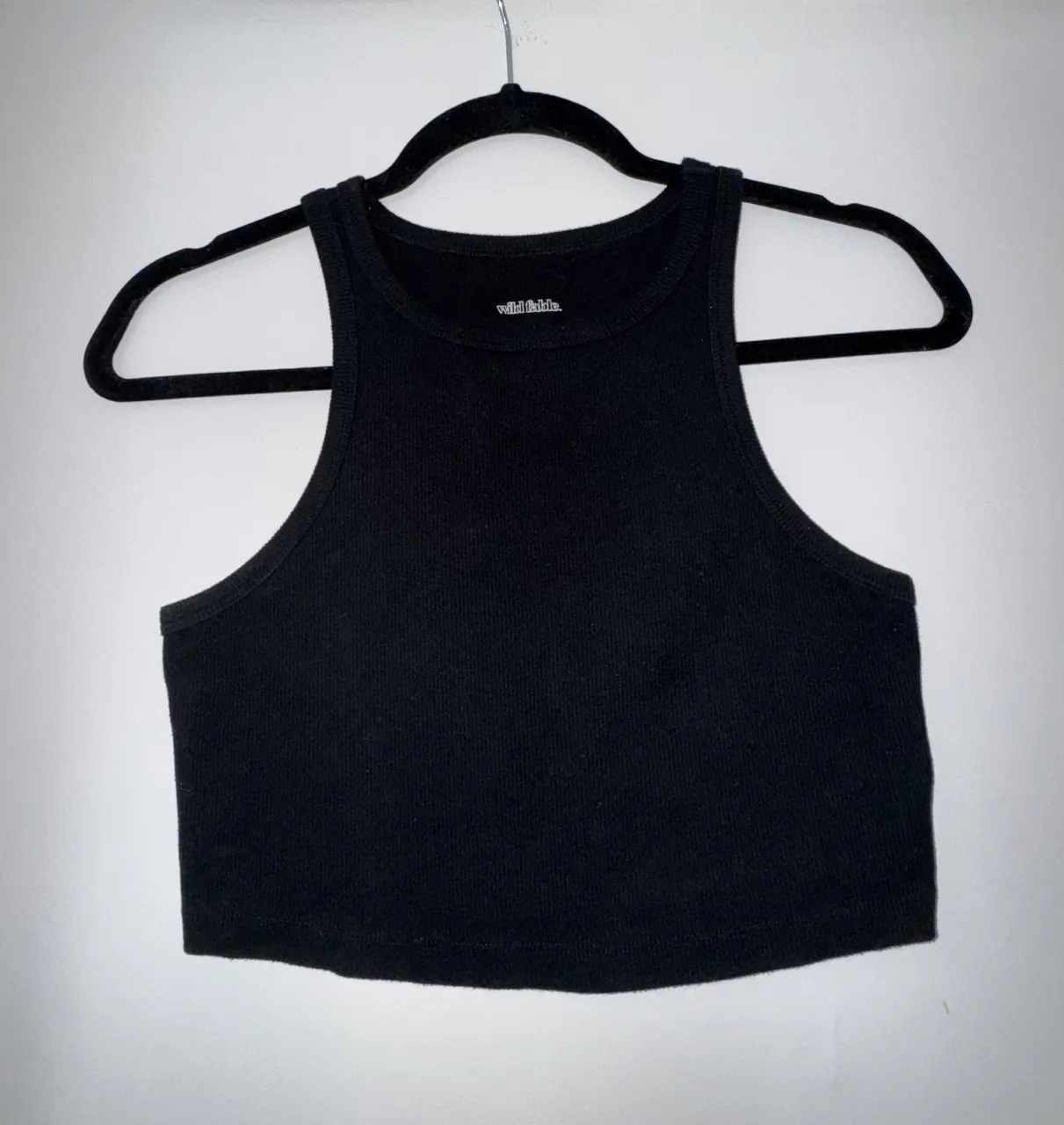Top negro de mujer, estilo musculosa, con cuello redondo y corte crop. Ideal para un look casual y moderno.