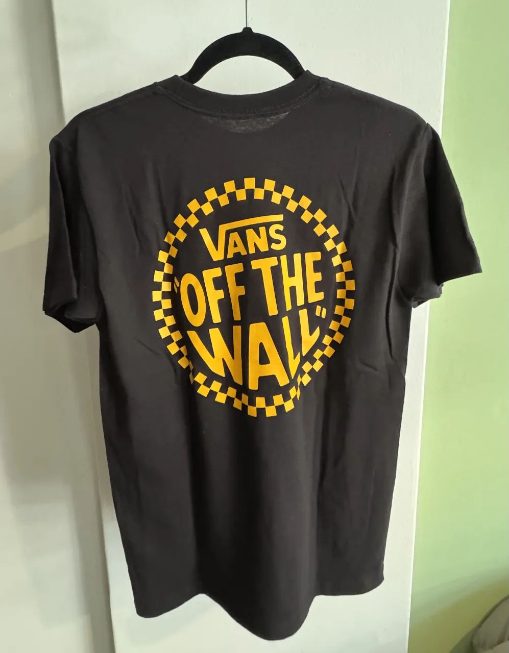 Remera negra de hombre con estampado "Off The Wall" de Vans en amarillo. Cuello redondo y manga corta. Ideal para un look casual y urbano.