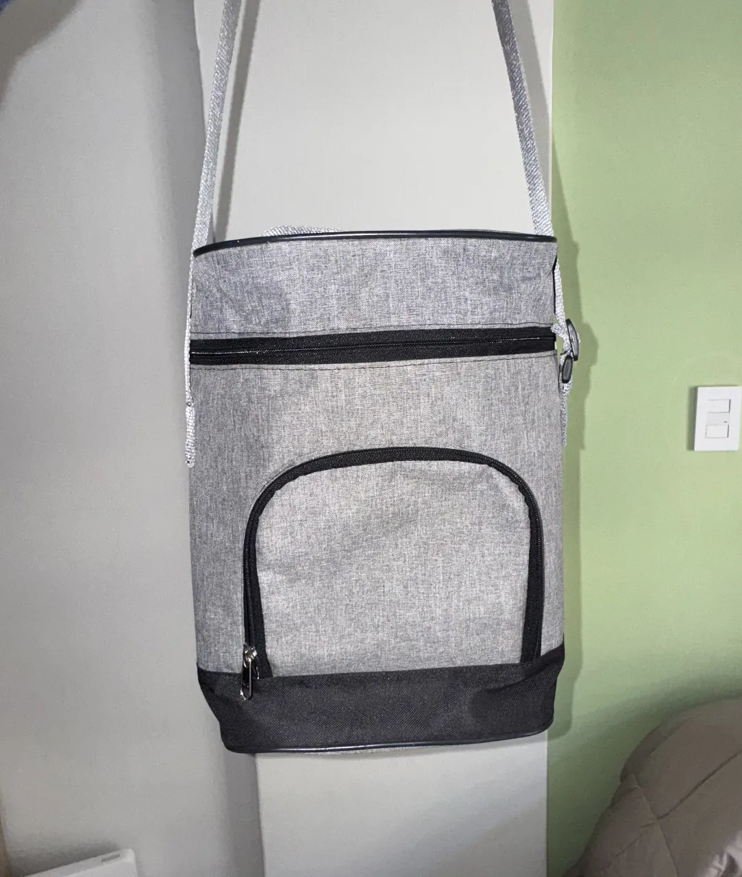 Matera gris . Bolsillo frontal , compartimiento con velcro interior, cierre y una correa ajustable para llevar al hombro.