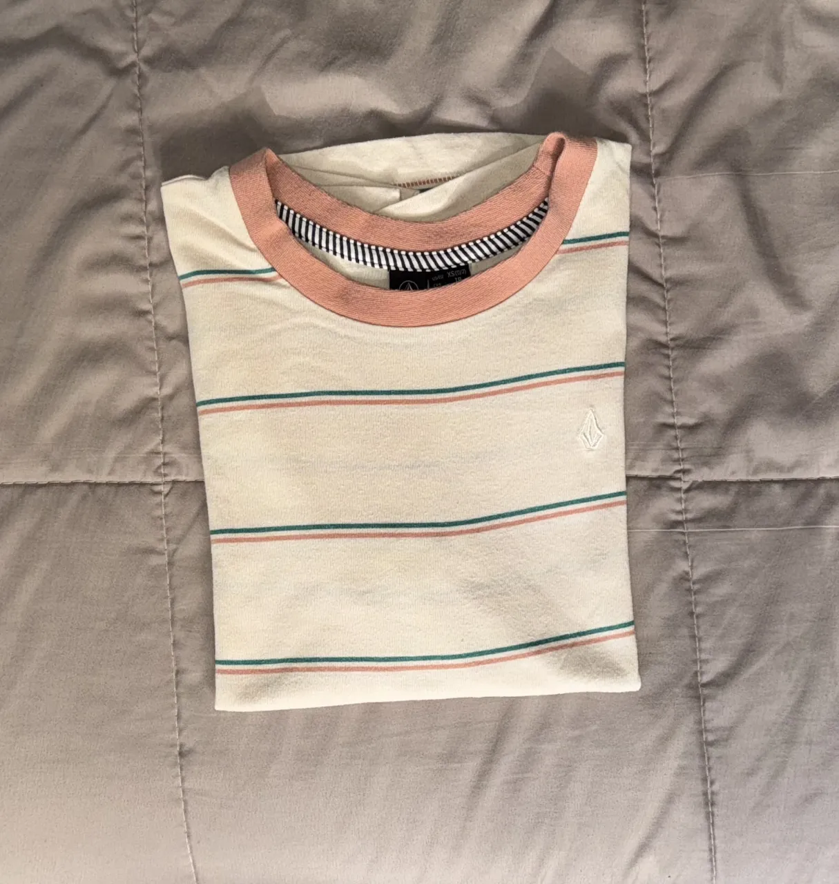 Remera de mujer Volcom a rayas horizontales en color crema con detalles en rosa y verde. Cuello redondo con borde en rosa y logo de la marca bordado.
