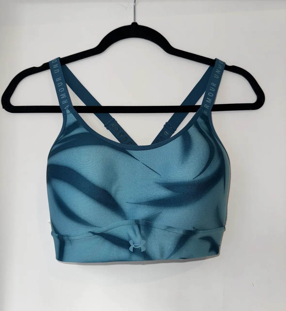 Top deportivo Under Armour para mujer, con diseño estampado en tonos azules. Ideal para actividades de alto impacto. Con desgastes unicamente en la inscripcion “under armour” de la espalda