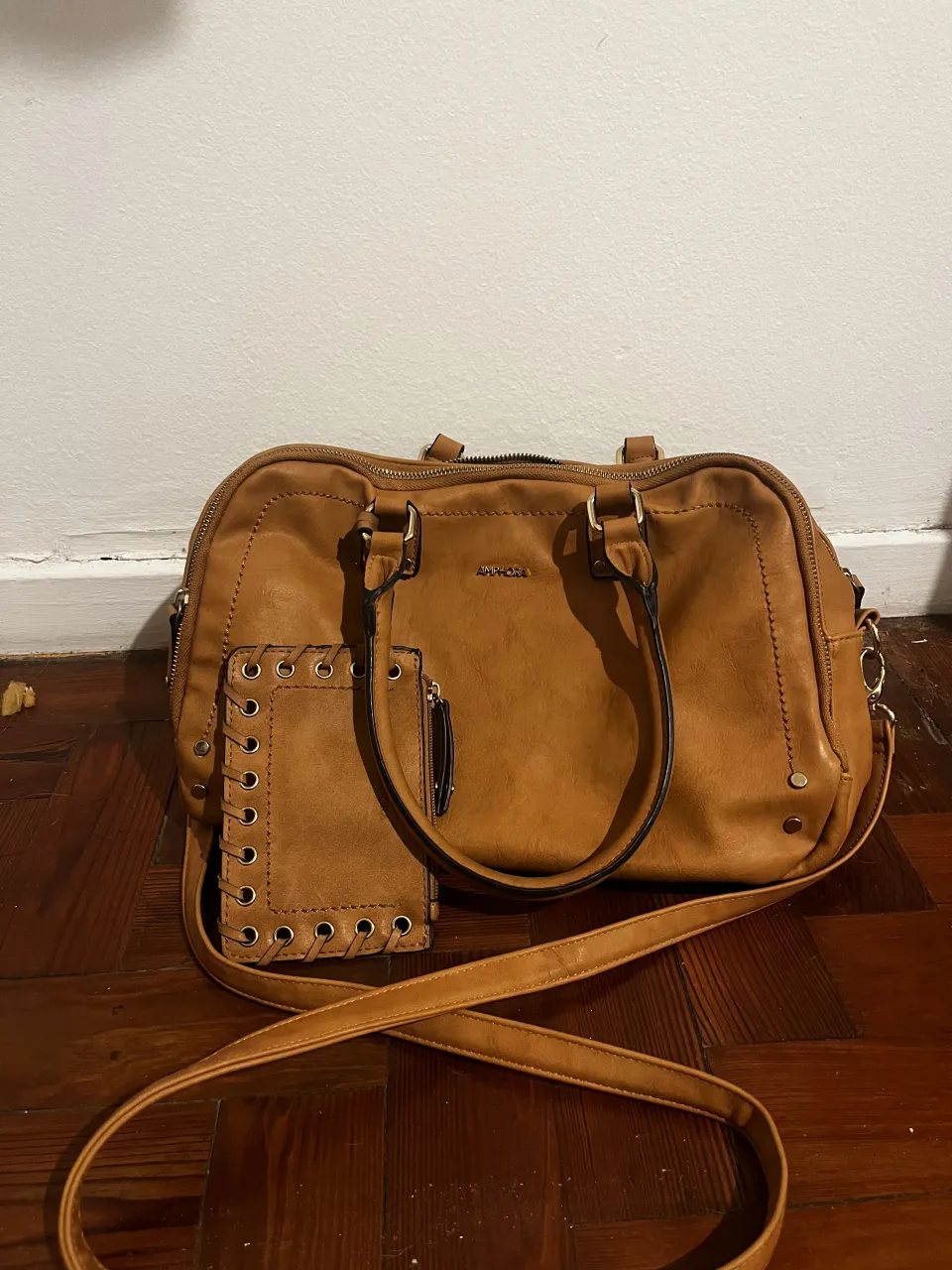 Bolso marrón de cuero sintético con correa larga desmontable. Incluye un pequeño monedero o tarjetero a juego con ojales y cordones decorativos. El interior del bolso tiene un forro estampado.