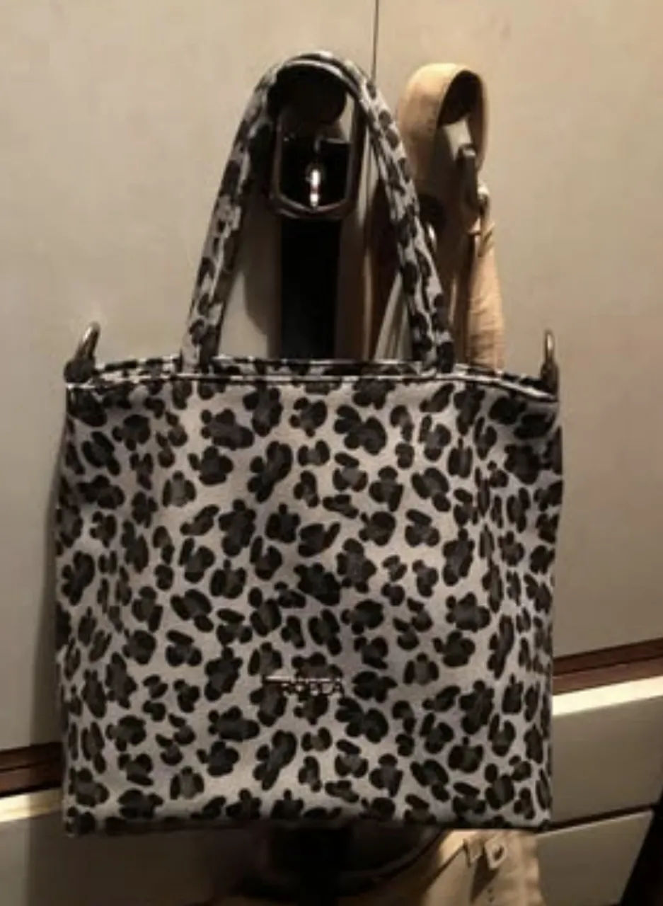 Cartera mediana tipo tote bag con estampado de leopardo en tonos grises y negros. No tiene la correa larga. Está forrada y tiene cierre superior. En su interior, tiene un bolsillo con cierre. La marca es Tropea.