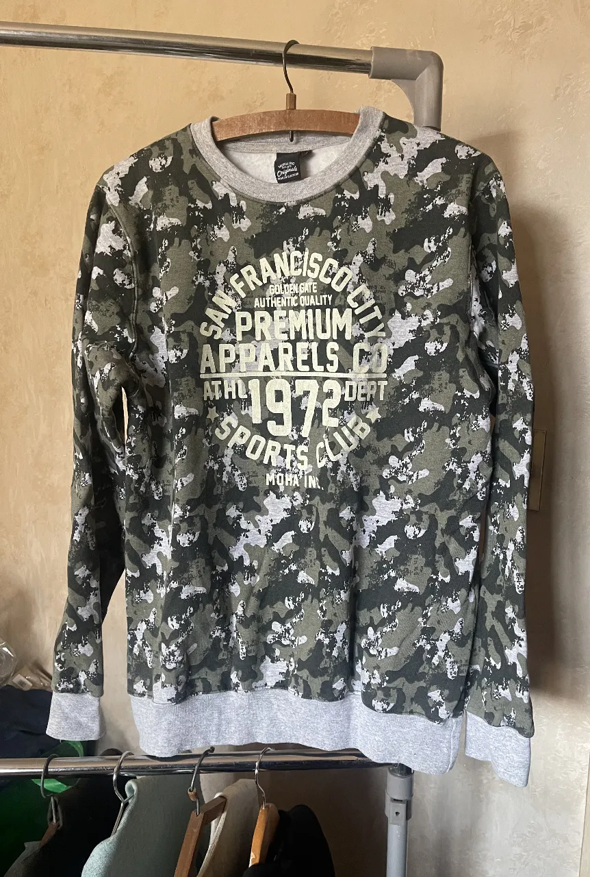 Buzo unisex con estampado camuflado y detalles en gris. Marca Moha Inc. Talle M. Ideal para un look casual y canchero.