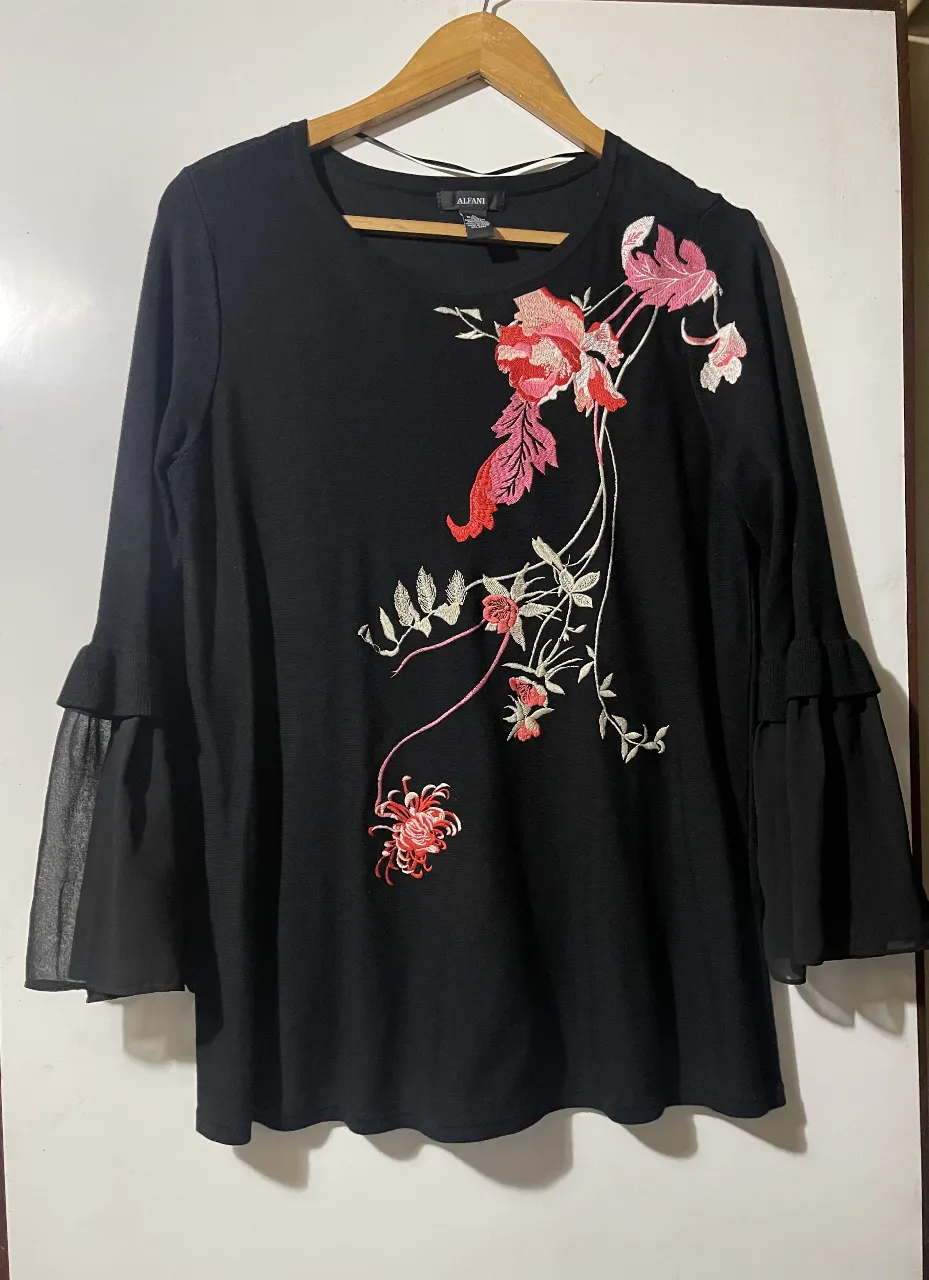 Sweater lanilla Alfani negro de manga larga, con detalles florales bordados en tonos rosa y blanco. Mangas acampanadas con volados de tela transparente. Ideal para un look elegante y femenino.