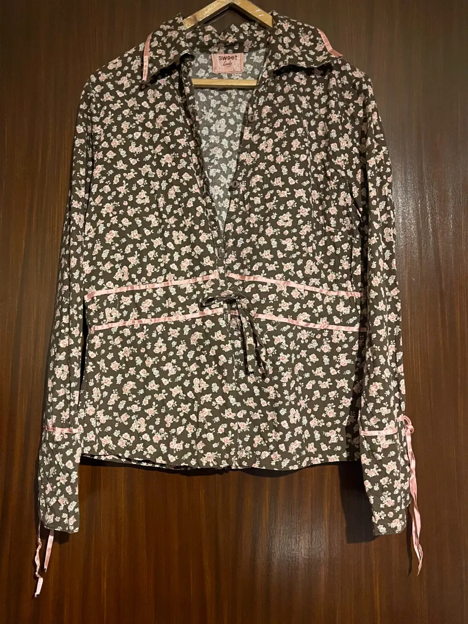 Camisa estampada con flores en tonos marrones y rosas. Tiene detalles en rosa en los bordes y lazos en las mangas. Ideal para un look vintage.