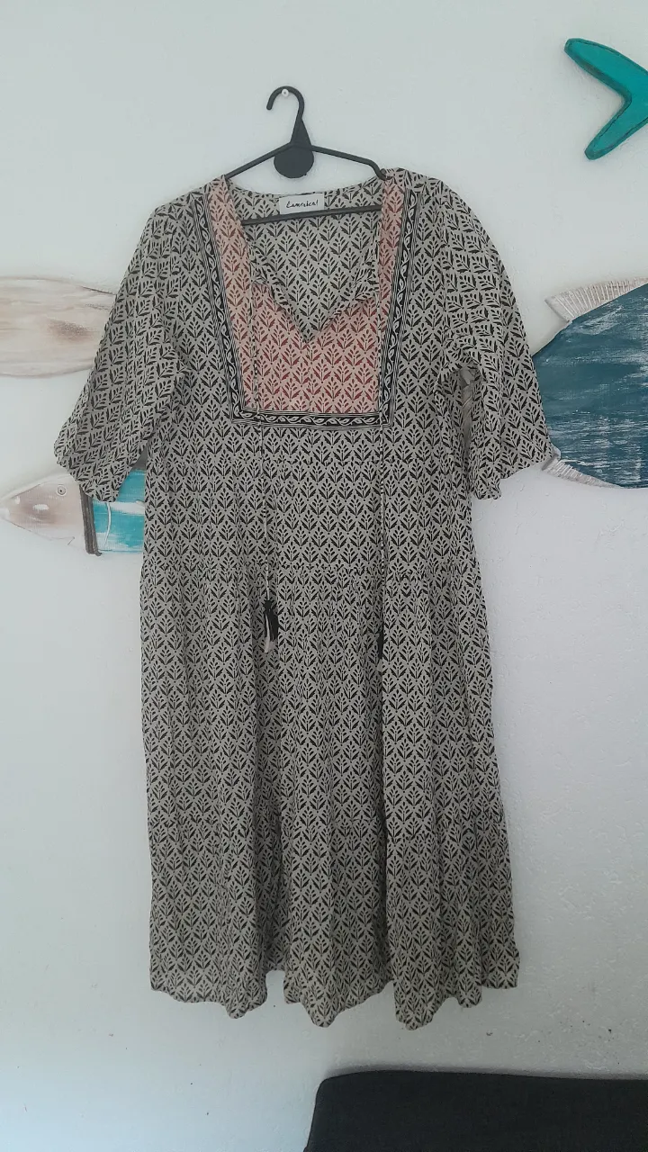 Vestido estampado con cuello en V y mangas cortas. Posee detalles bordados en la parte superior del busto y dos tiras finas con pompones en la cintura.