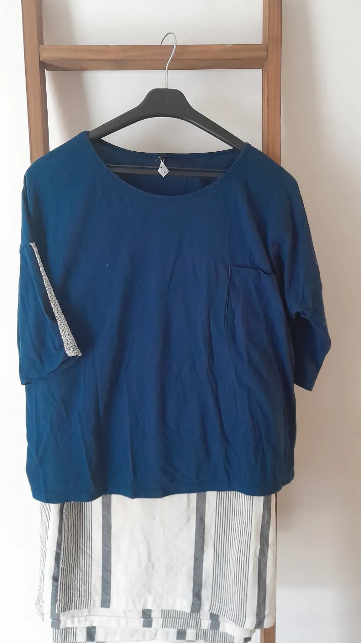 Remera azul de manga corta con detalles de tejido plateado en las mangas. Tiene un bolsillo en el frente y un corte moderno.