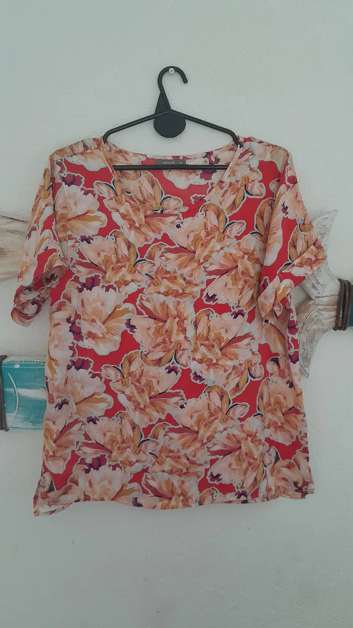 Remera estampada con flores en tonos rojos, naranjas y blancos. Posee mangas cortas y cuello en V.