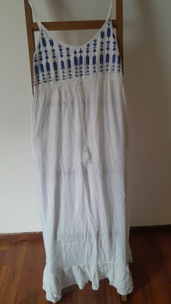 Vestido largo blanco con bordado azul en la parte superior y volados en el ruedo. Posee un cordón ajustable en la cintura.