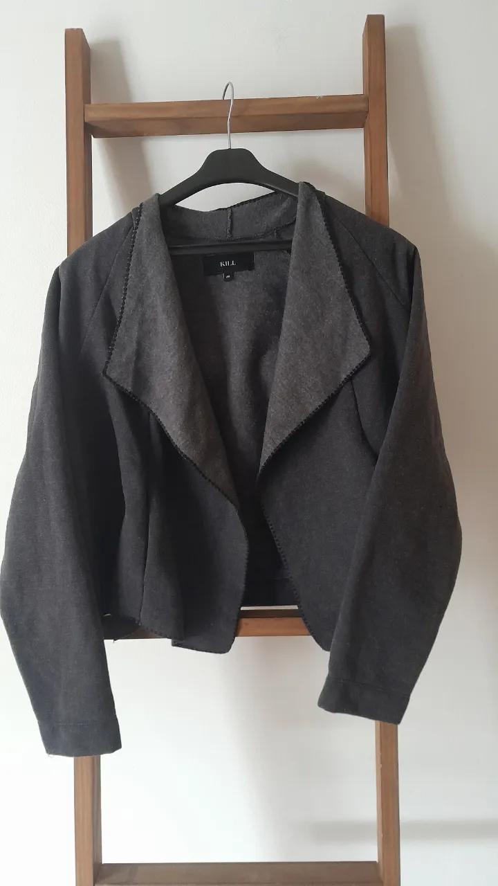 Chaqueta corta de paño gris oscuro, con cuello solapa y bolsillos laterales. Ideal para un look casual o elegante.
