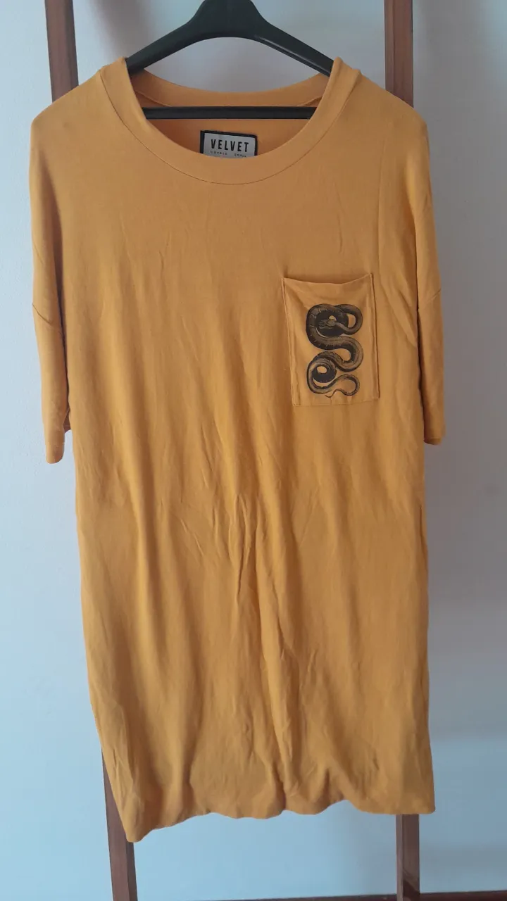 Remera amarilla de manga corta con estampa de serpiente en el bolsillo. Ideal para un look casual y moderno.