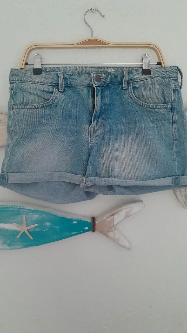 Shorts de jean tiro regular, color azul claro con efecto desgastado y dobladillo en el borde inferior.
