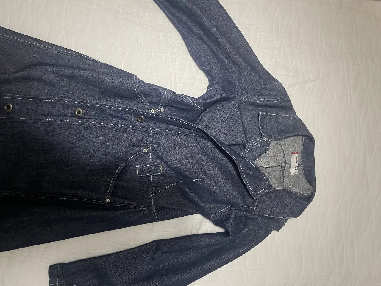 Campera larga de jean azul oscuro, estilo trench, con detalles de costuras en blanco. Ideal para un look casual y moderno.