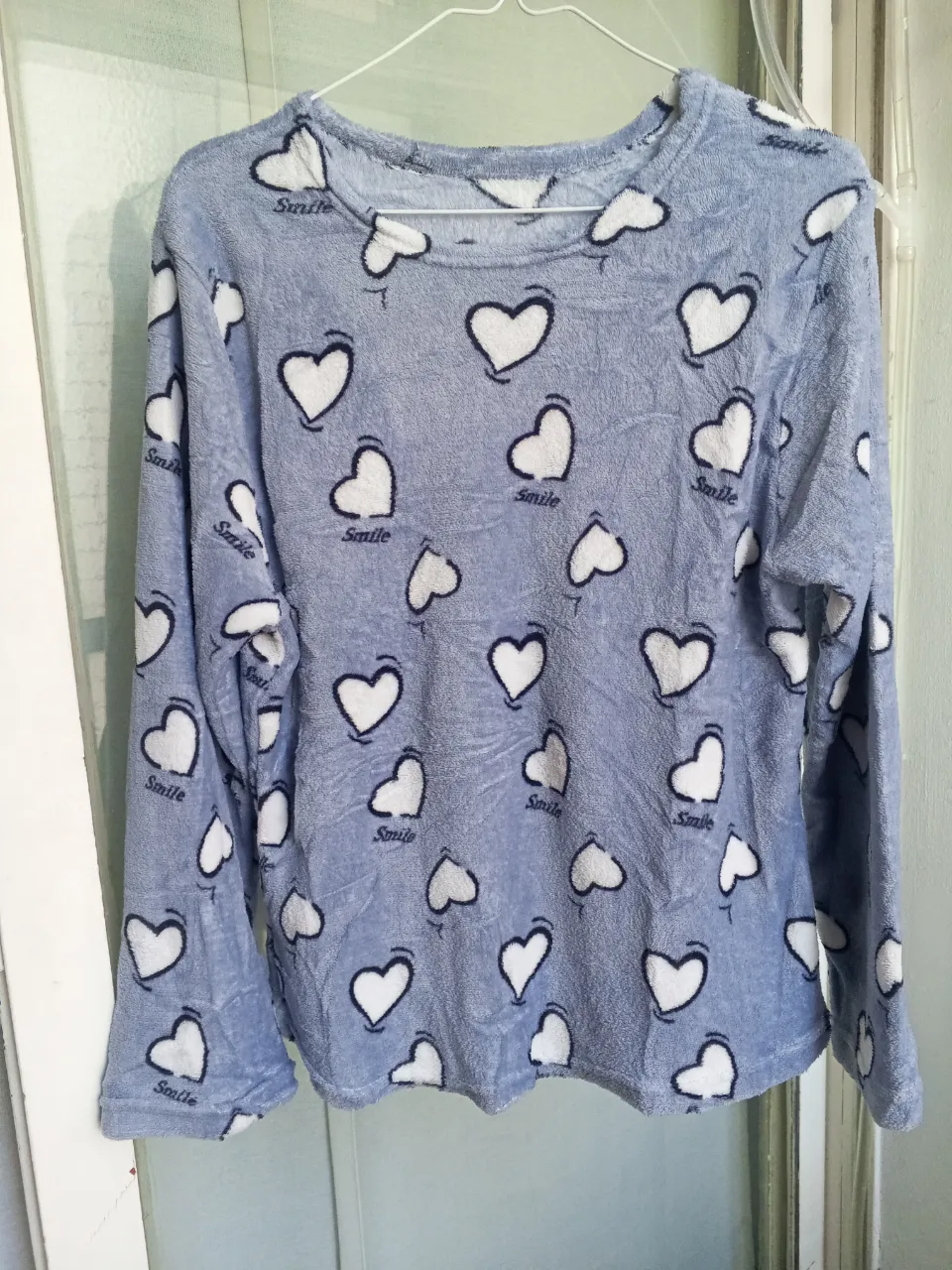 Buzo con estampa de corazones blancos y la palabra "Smile" en negro sobre fondo celeste. La tela es suave y con textura. Ancho 45 cm / largo 62 cm.