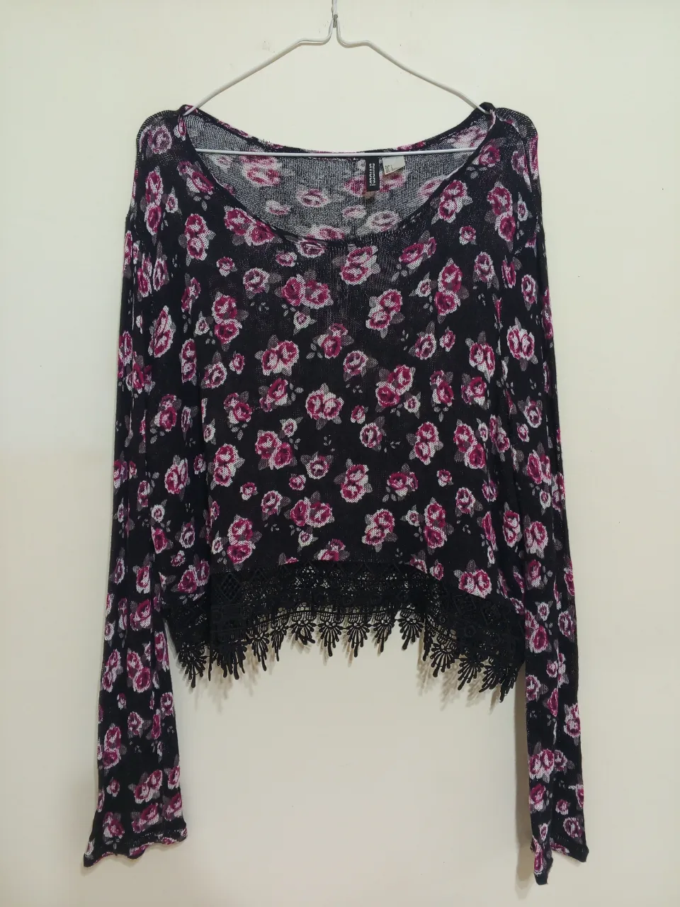 Remera manga larga estampada con flores rosas y detalles de encaje en el borde inferior. Ideal para un look casual y femenino.