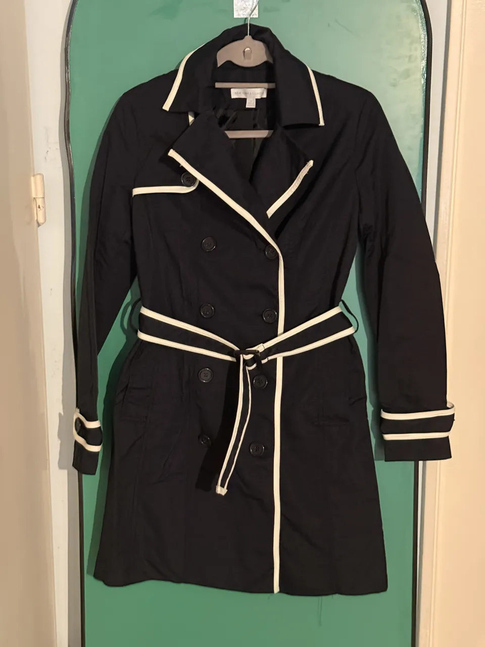 Tapado negro con vivos blancos en cuello, puños y cinturón. Doble abotonadura.