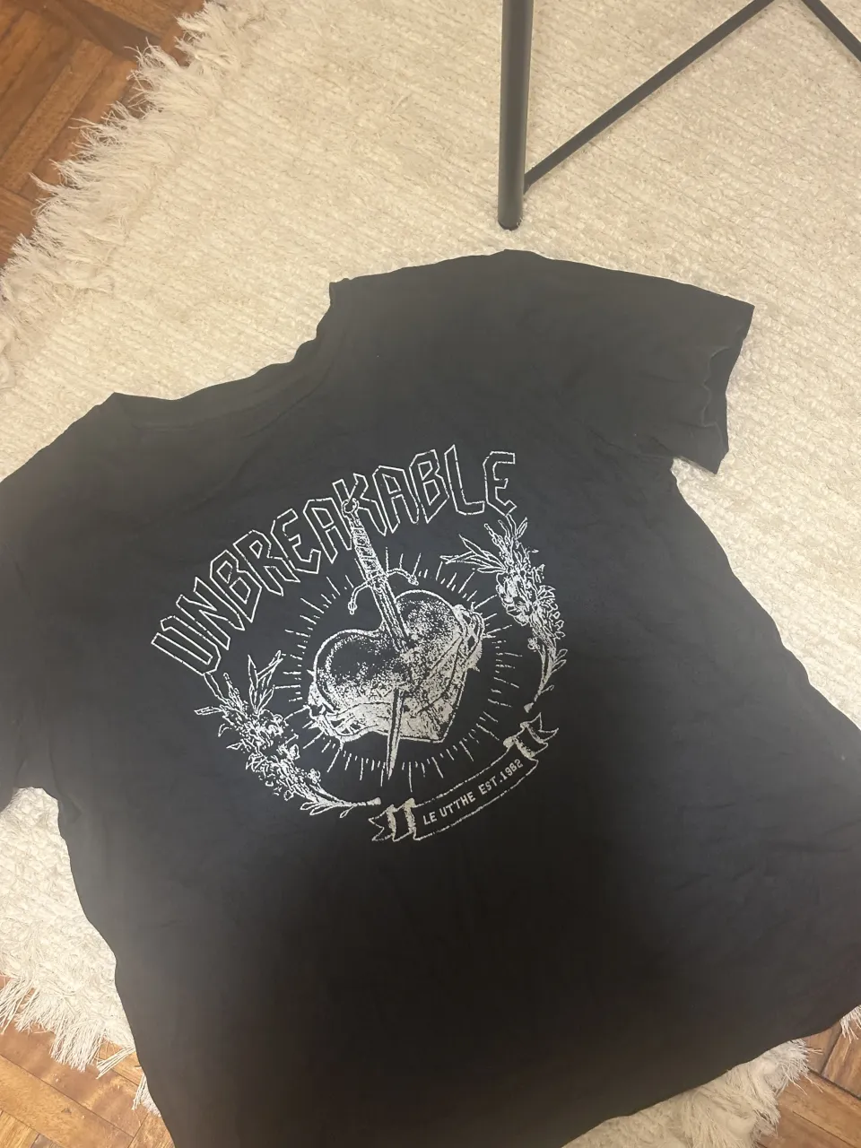 Remera negra con estampa "UNBREAKABLE" y un corazón atravesado por una espada. Ideal para un look rocker o casual.