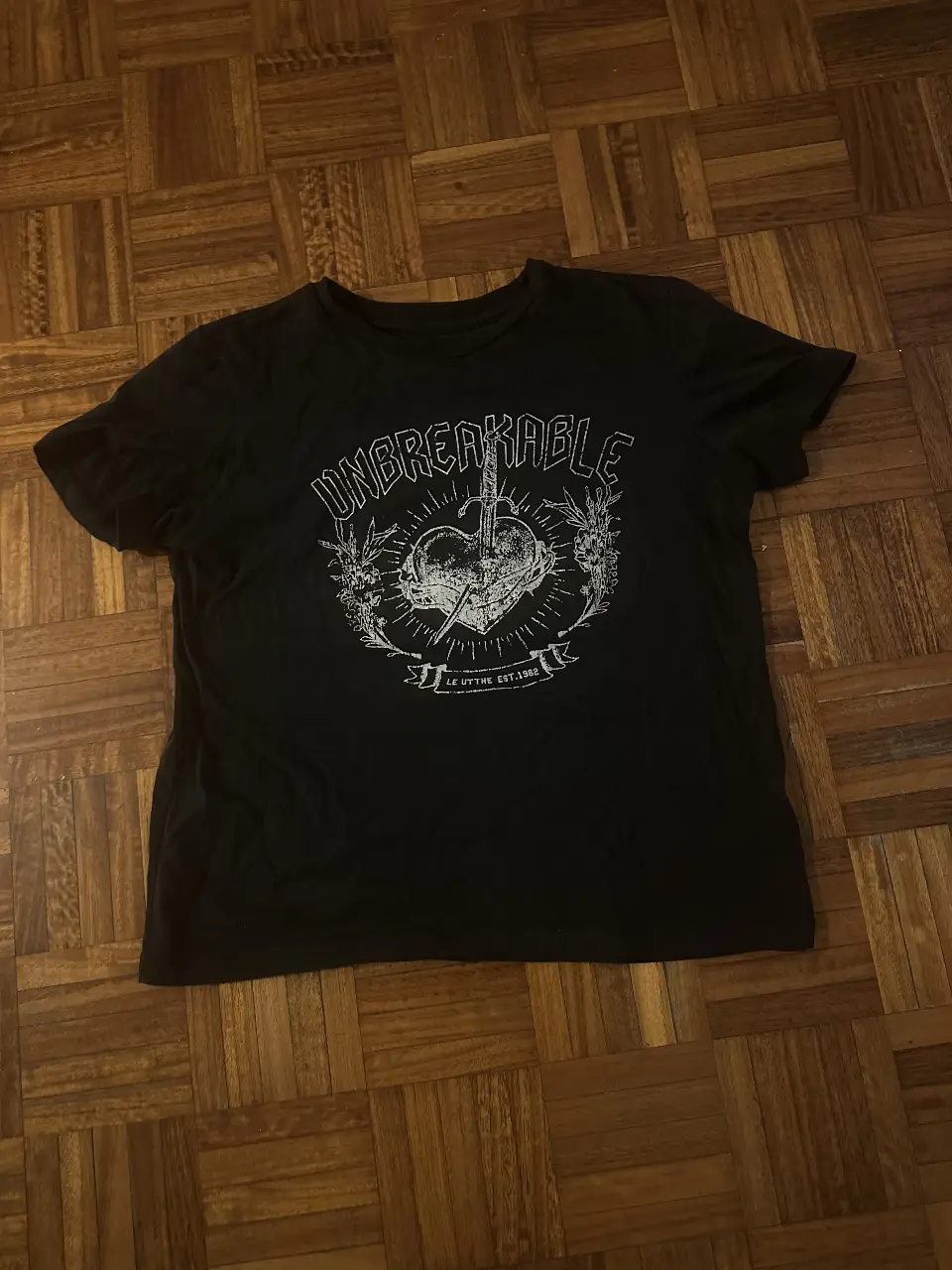 Remera negra de manga corta con estampado "Unbreakable" en blanco. Talle XXS de la marca Le Utthe, Industria Argentina. Ideal para un look rocker o casual.