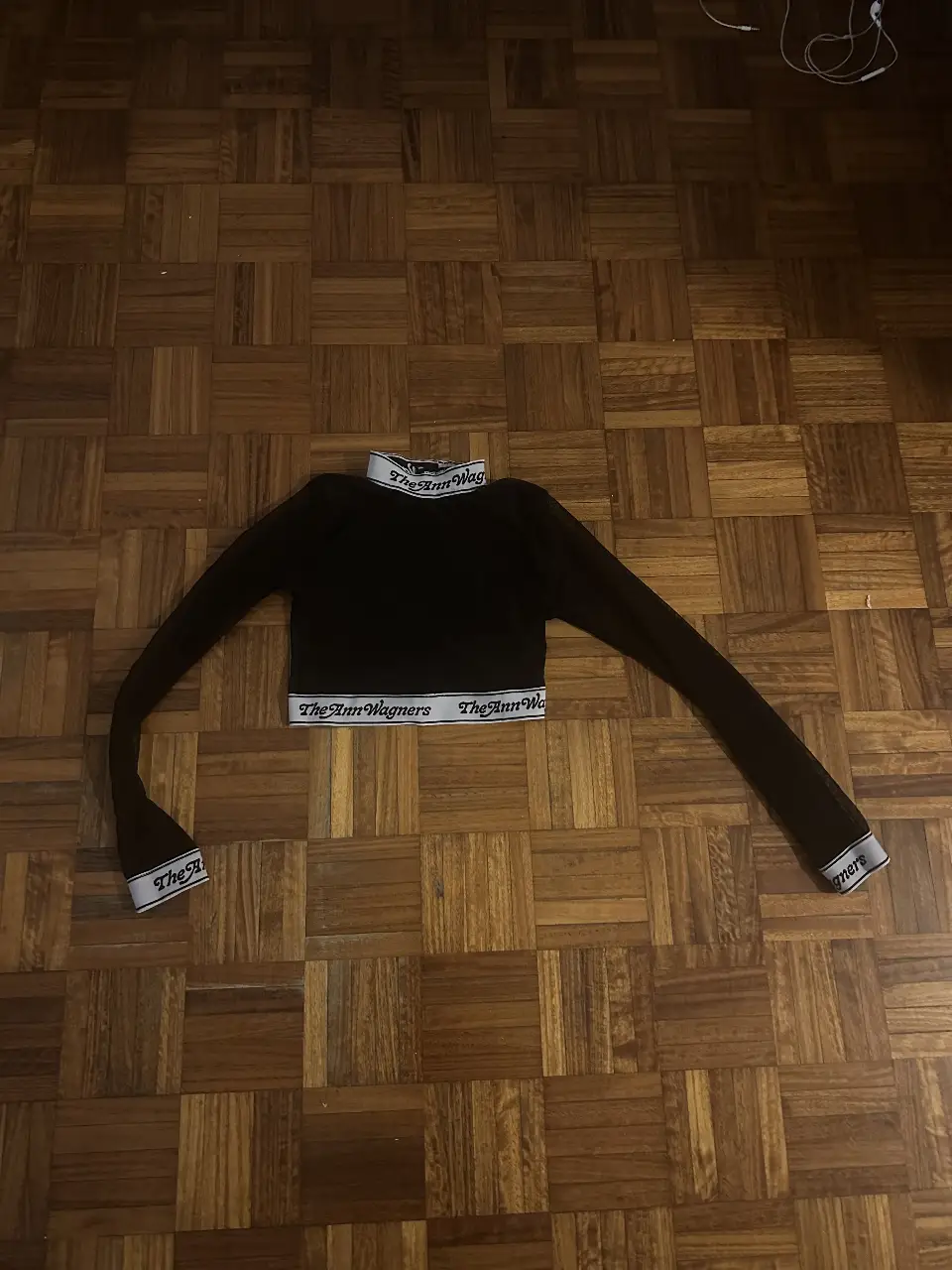 Top manga larga negro con detalles en blanco. Cuello alto y cintura con la inscripción "The Ann Wagners". Ideal para un look moderno y audaz.