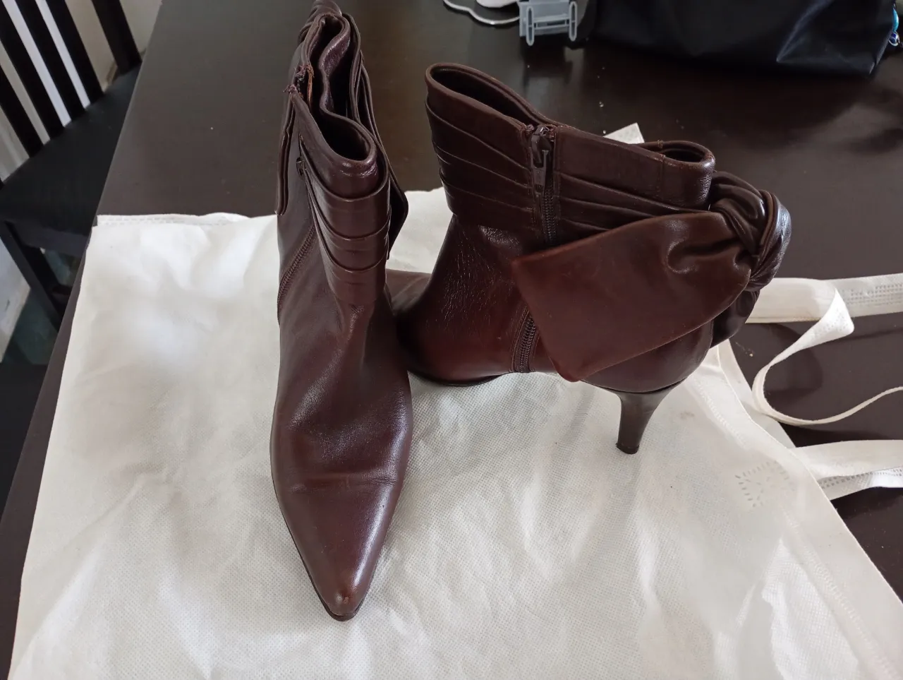 Botitas de cuero color marrón oscuro, con taco fino y detalle de moño en la parte trasera. Cierre lateral.