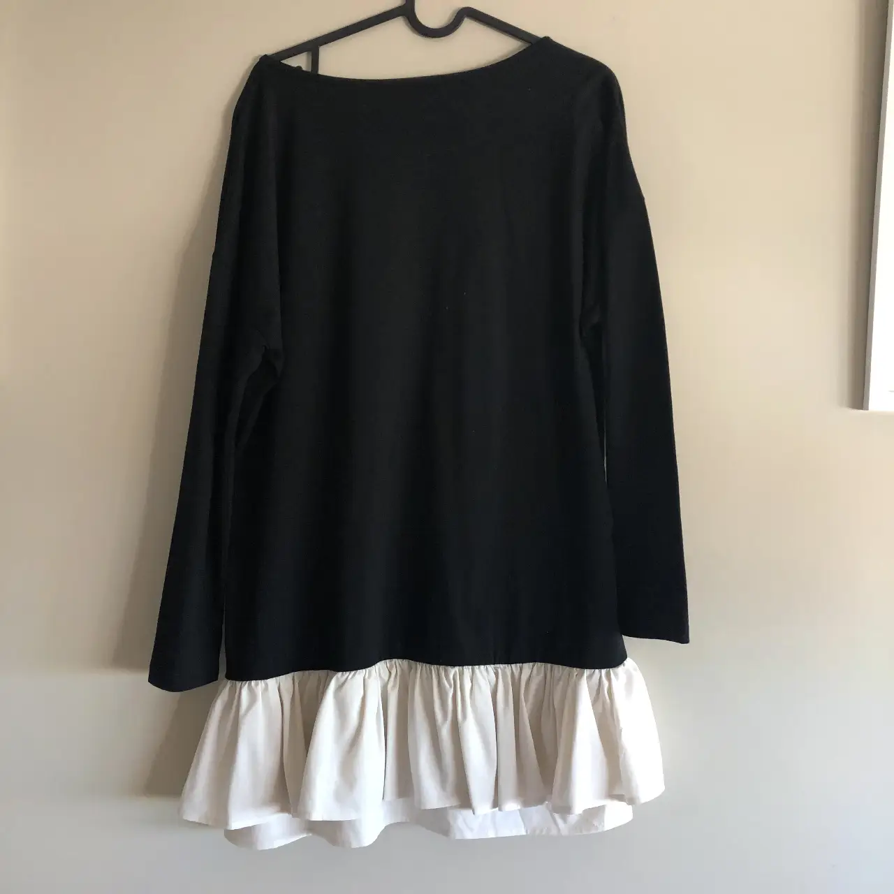 Vestido midi negro con detalle de volados blancos en el bajo. Manga larga y cuello redondo. Ideal para un look casual y moderno.