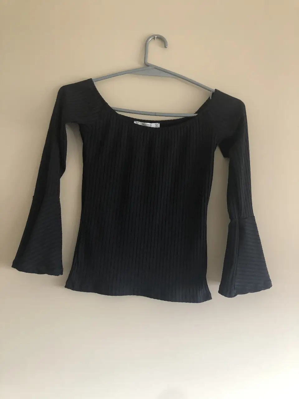 Blusa negra de manga larga con mangas acampanadas, ideal para un look elegante y moderno. Confeccionada en tejido de punto acanalado, ofrece un ajuste favorecedor y cómodo. Perfecta para combinar con pantalones de vestir o faldas.