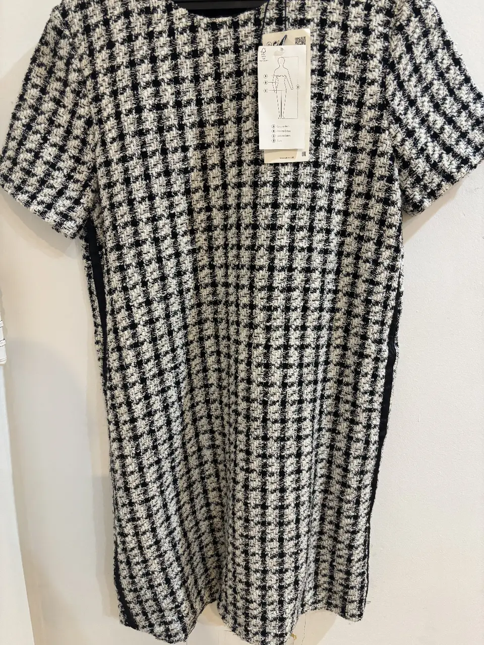 Vestido mini de tela tweed en blanco y negro, con mangas cortas y cierre en la espalda. Ideal para un look elegante y moderno.