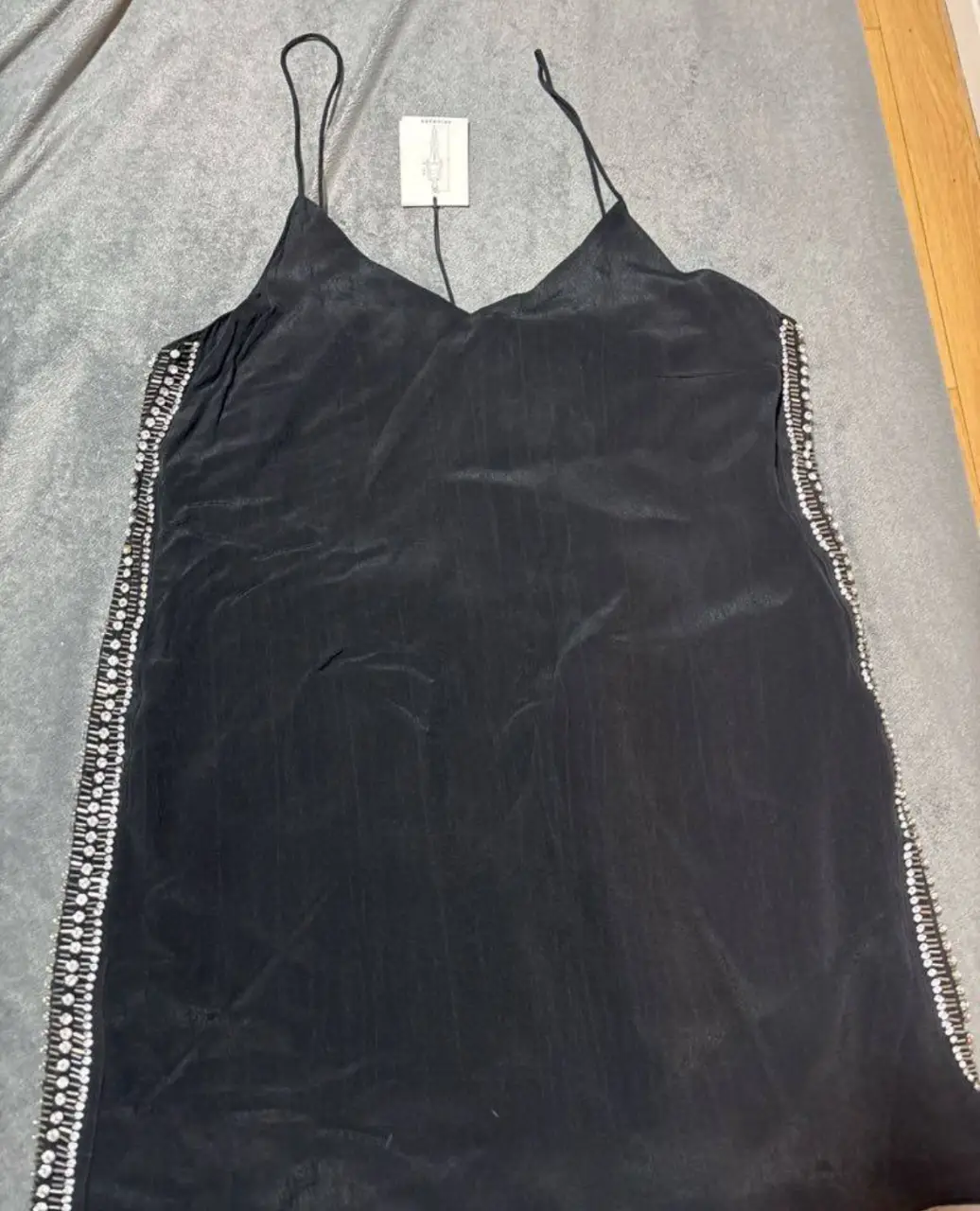 Vestido mini negro con tirantes finos y detalles de pedrería en los laterales. Ideal para una fiesta o evento especial.