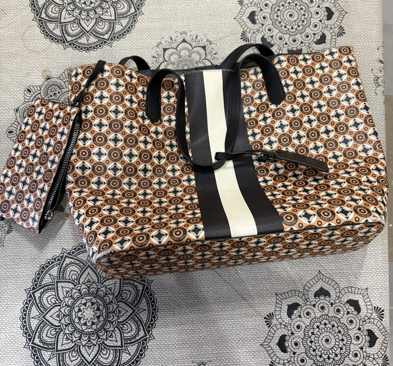 Bolso tote con estampado geométrico en tonos marrones y blancos, con detalles en negro. Incluye un neceser a juego con cierre. Ideal para llevar todo lo necesario con estilo.